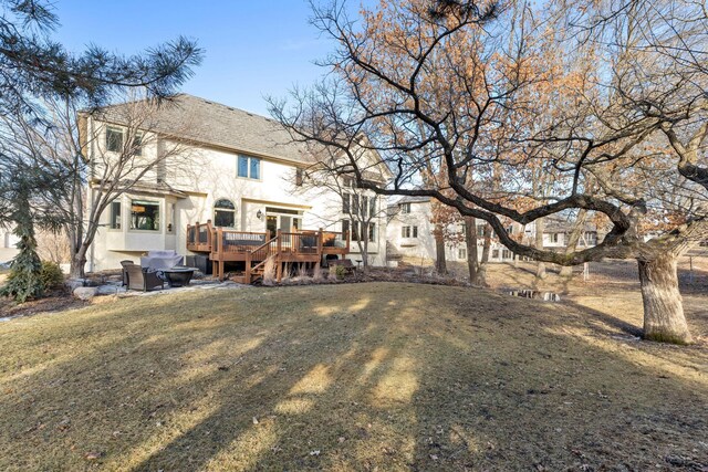 rear view of property with a lawn, a wooden deck, and stucco siding