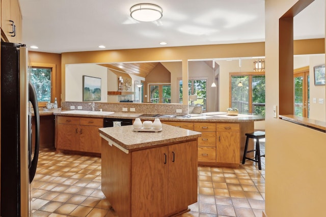 kitchen with kitchen peninsula, stainless steel fridge, lofted ceiling, a kitchen bar, and a kitchen island