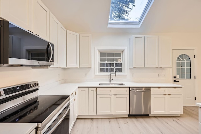 kitchen featuring sink, a skylight, light hardwood / wood-style floors, white cabinetry, and stainless steel appliances