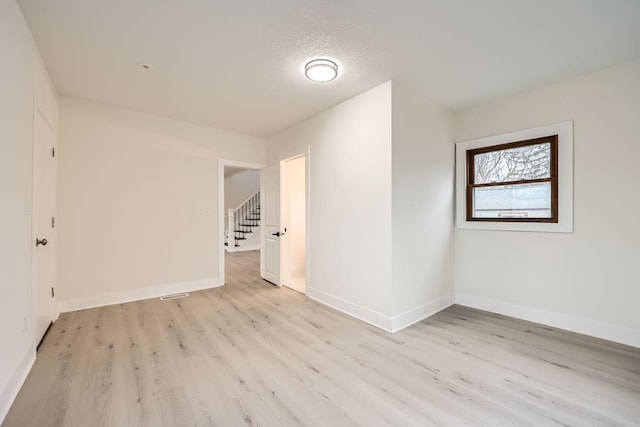 empty room with a textured ceiling and light hardwood / wood-style flooring