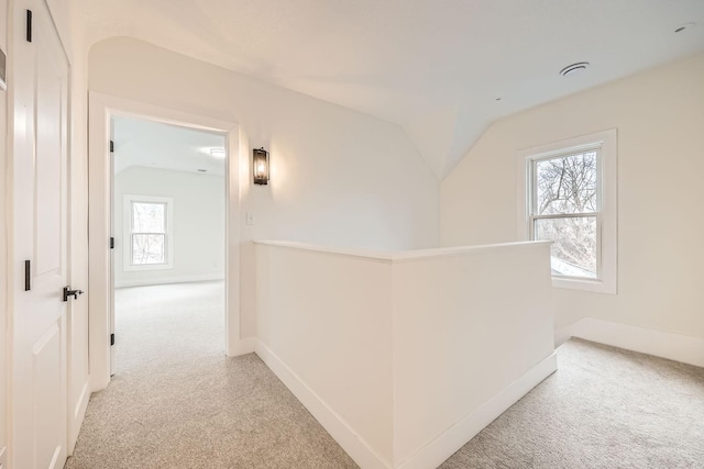 hallway with lofted ceiling, light colored carpet, and a healthy amount of sunlight