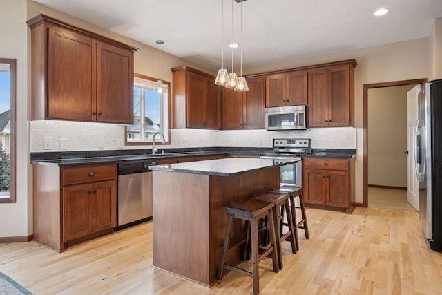 kitchen featuring a kitchen island, pendant lighting, a breakfast bar area, stainless steel appliances, and light hardwood / wood-style flooring