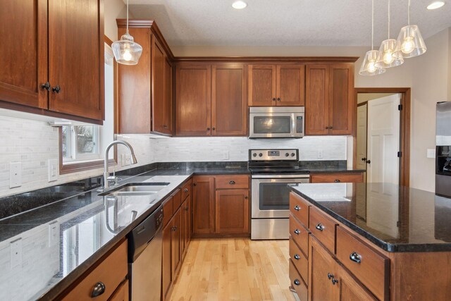 kitchen featuring decorative light fixtures, sink, dark stone countertops, stainless steel appliances, and light wood-type flooring