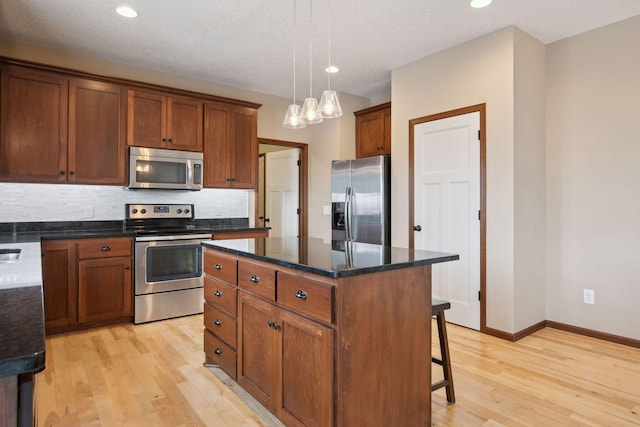 kitchen with pendant lighting, decorative backsplash, a center island, light hardwood / wood-style floors, and stainless steel appliances