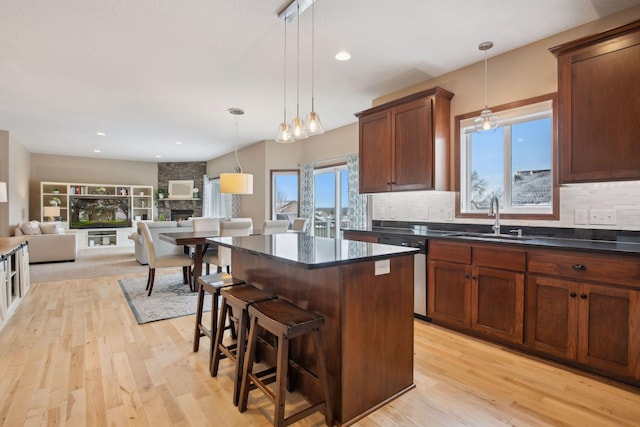 kitchen with sink, light wood-type flooring, a kitchen breakfast bar, pendant lighting, and a fireplace