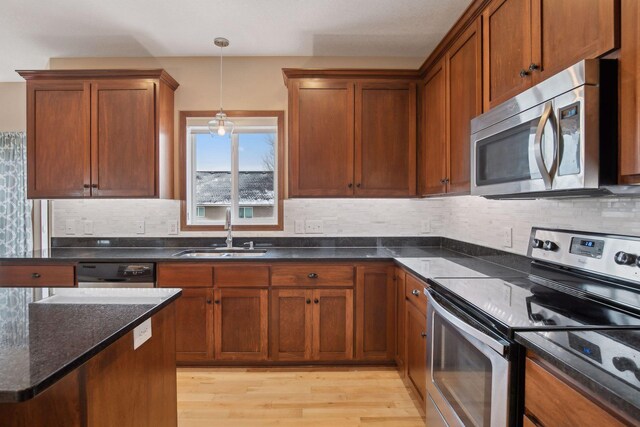 kitchen featuring sink, appliances with stainless steel finishes, dark stone countertops, light hardwood / wood-style floors, and decorative light fixtures