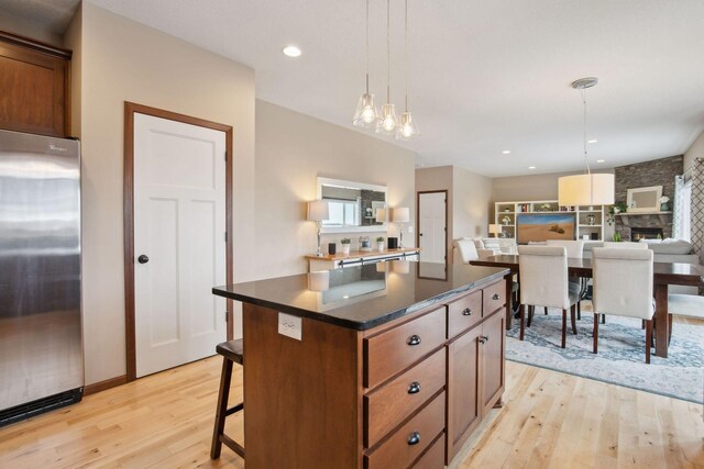 kitchen with a breakfast bar area, decorative light fixtures, light wood-type flooring, stainless steel fridge, and a kitchen island