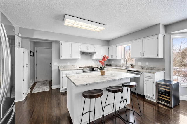 kitchen featuring a kitchen bar, stainless steel appliances, beverage cooler, a kitchen island, and white cabinets