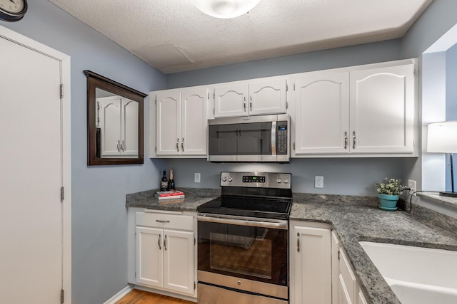 kitchen with white cabinets, sink, a textured ceiling, appliances with stainless steel finishes, and light hardwood / wood-style floors