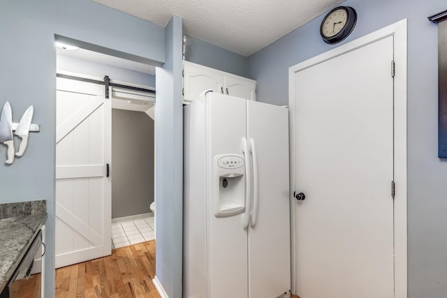 kitchen with white refrigerator with ice dispenser, light hardwood / wood-style flooring, a barn door, a textured ceiling, and white cabinetry