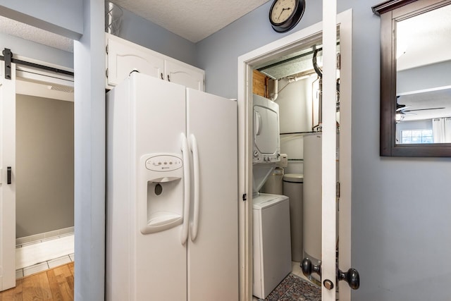 washroom with ceiling fan, a barn door, a textured ceiling, light hardwood / wood-style floors, and stacked washer / dryer