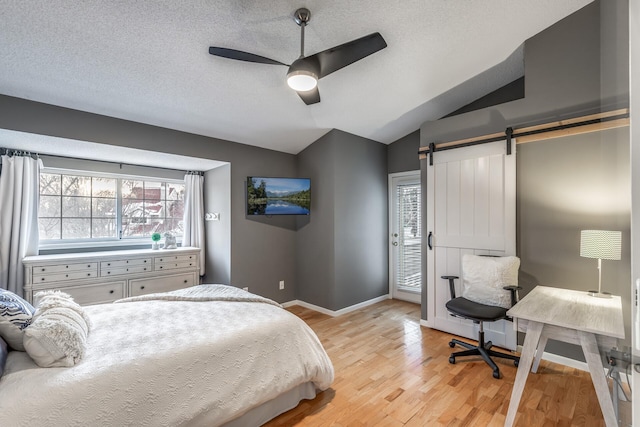 bedroom with ceiling fan, a barn door, light hardwood / wood-style flooring, multiple windows, and lofted ceiling