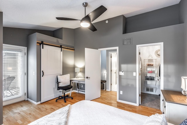 bedroom featuring light wood-type flooring, ceiling fan, a barn door, multiple windows, and lofted ceiling