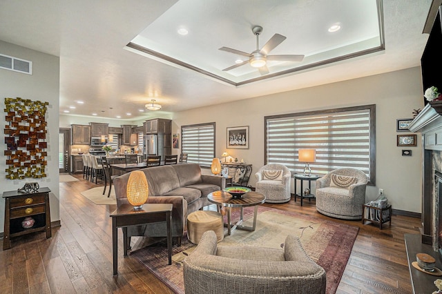 living room featuring a tray ceiling, a tiled fireplace, and dark hardwood / wood-style flooring