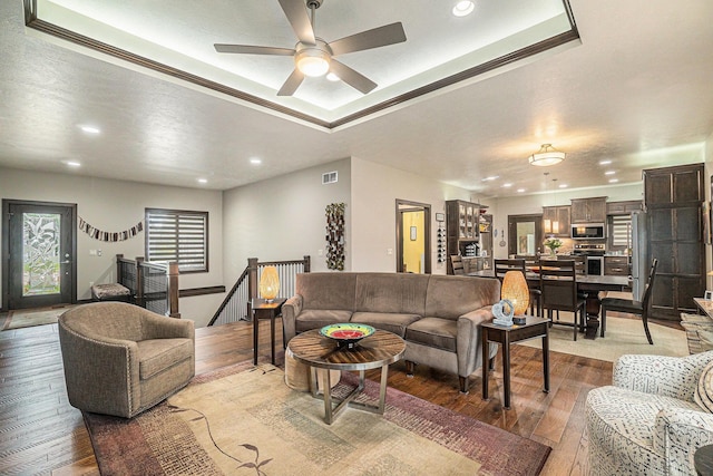 living room featuring a raised ceiling, crown molding, hardwood / wood-style floors, and ceiling fan