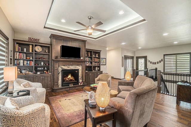 living room featuring ceiling fan, dark hardwood / wood-style flooring, a high end fireplace, and a tray ceiling