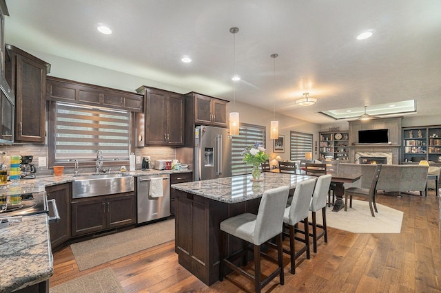 kitchen with appliances with stainless steel finishes, a kitchen island, hanging light fixtures, and wood-type flooring