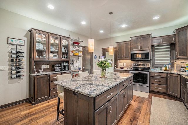 kitchen featuring appliances with stainless steel finishes, light stone counters, dark brown cabinets, dark wood-type flooring, and pendant lighting