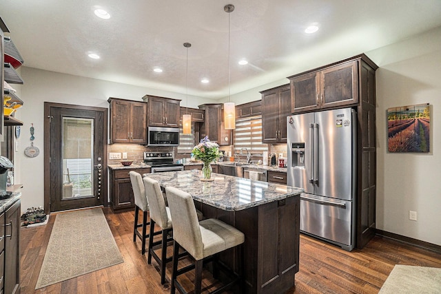 kitchen with a wealth of natural light, a kitchen island, stainless steel appliances, and hanging light fixtures