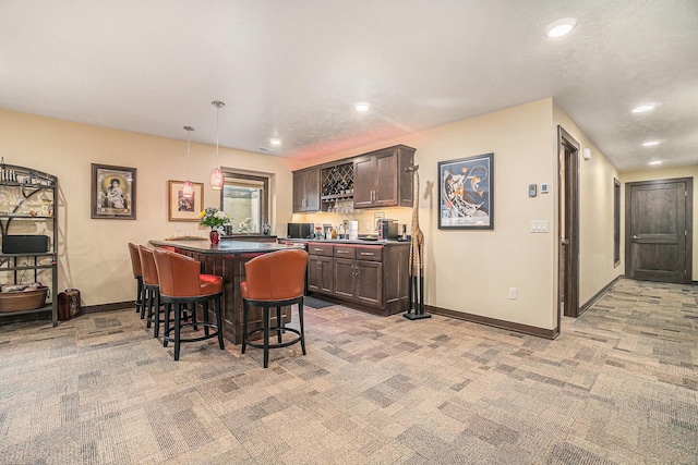 interior space featuring a kitchen breakfast bar, dark brown cabinetry, light colored carpet, pendant lighting, and a center island