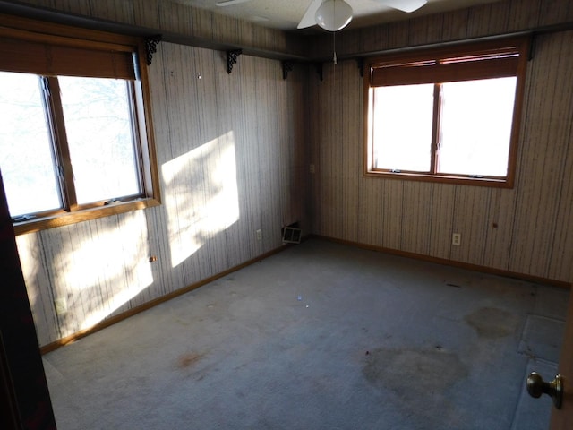 empty room with ceiling fan, wood walls, and light carpet