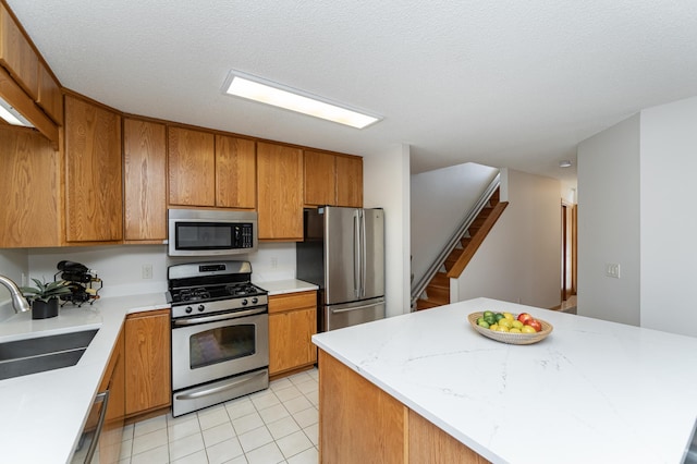 kitchen featuring sink, light tile patterned floors, appliances with stainless steel finishes, a center island, and a textured ceiling