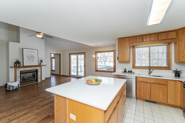 kitchen featuring sink, a center island, vaulted ceiling, stainless steel dishwasher, and a tiled fireplace