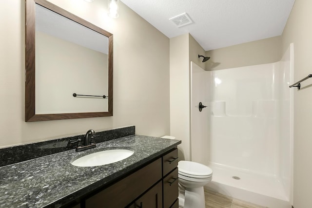 bathroom with a textured ceiling, vanity, toilet, and a shower