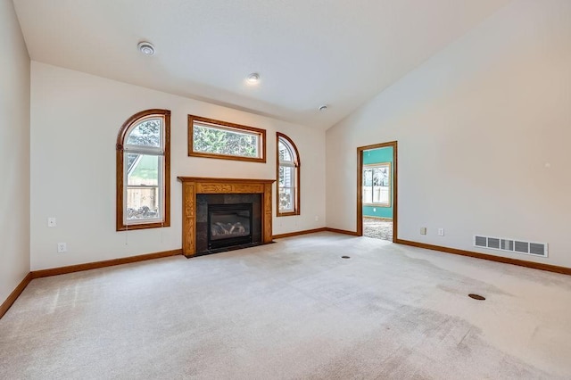 unfurnished living room featuring light carpet, high vaulted ceiling, a fireplace, and a healthy amount of sunlight