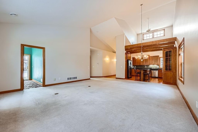 unfurnished living room featuring a chandelier, light carpet, high vaulted ceiling, and a healthy amount of sunlight