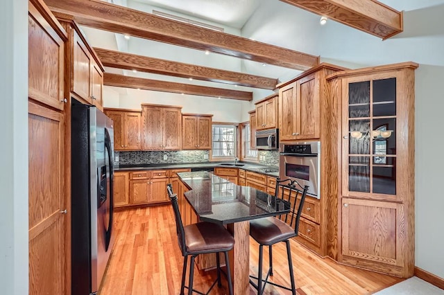 kitchen featuring a breakfast bar, light hardwood / wood-style floors, beamed ceiling, a kitchen island, and stainless steel appliances