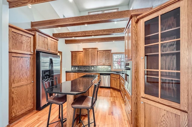 kitchen with a center island, a kitchen breakfast bar, dark stone counters, appliances with stainless steel finishes, and light wood-type flooring