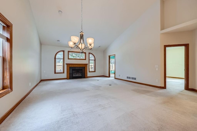 unfurnished living room with a tile fireplace, high vaulted ceiling, light colored carpet, and an inviting chandelier