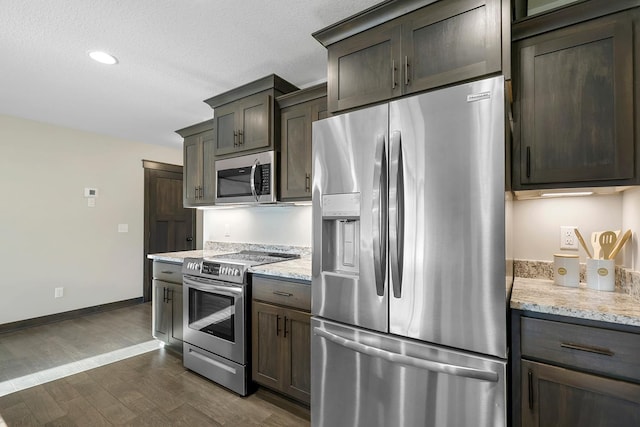 kitchen with light stone counters, dark wood-type flooring, a textured ceiling, and appliances with stainless steel finishes