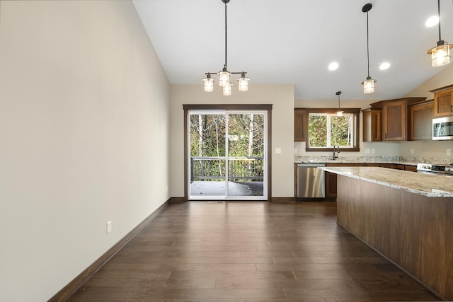 kitchen with lofted ceiling, light stone counters, decorative light fixtures, dark hardwood / wood-style flooring, and stainless steel appliances