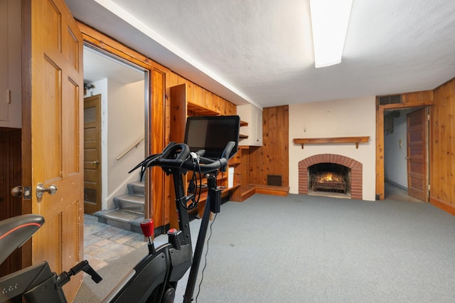 workout room with a textured ceiling, light colored carpet, a brick fireplace, and wood walls