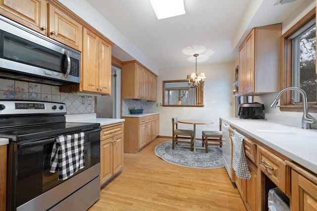 kitchen with sink, light hardwood / wood-style flooring, a notable chandelier, decorative light fixtures, and appliances with stainless steel finishes