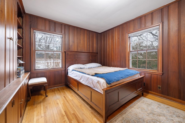 bedroom with light hardwood / wood-style flooring, multiple windows, and wood walls