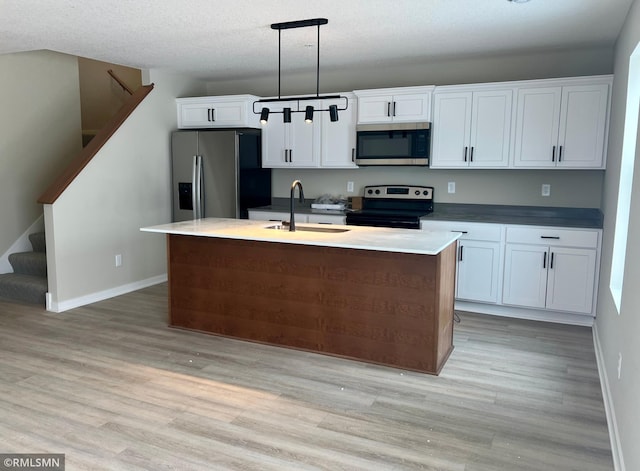 kitchen with appliances with stainless steel finishes, sink, hanging light fixtures, and an island with sink