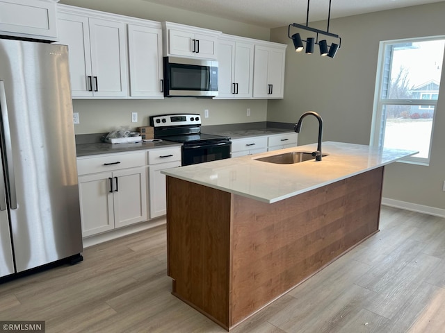 kitchen featuring white cabinetry, appliances with stainless steel finishes, decorative light fixtures, a kitchen island with sink, and sink