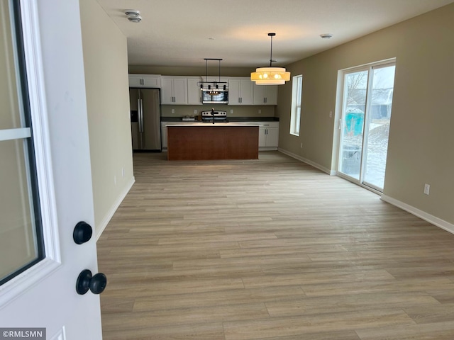 kitchen featuring white cabinets, stainless steel appliances, light hardwood / wood-style floors, hanging light fixtures, and a kitchen island with sink