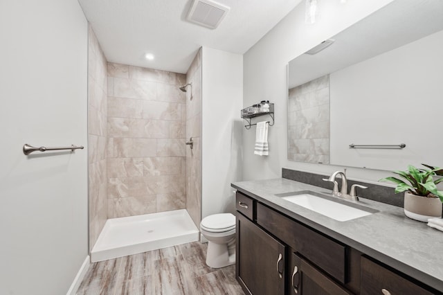 bathroom featuring a tile shower, toilet, vanity, and hardwood / wood-style flooring