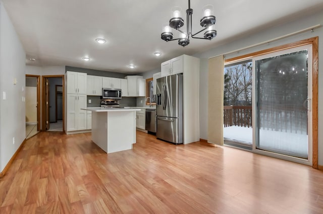 kitchen featuring white cabinetry, stainless steel appliances, a center island, decorative light fixtures, and light wood-type flooring