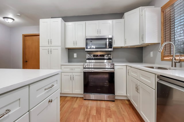 kitchen with sink, light wood-type flooring, white cabinets, and appliances with stainless steel finishes