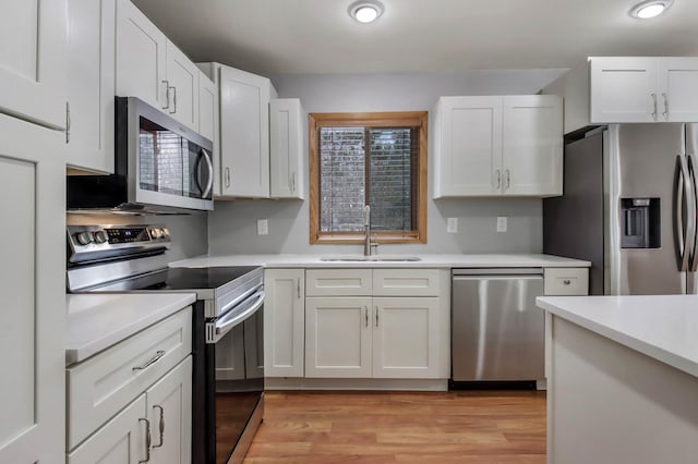 kitchen with appliances with stainless steel finishes, sink, white cabinets, and light hardwood / wood-style floors