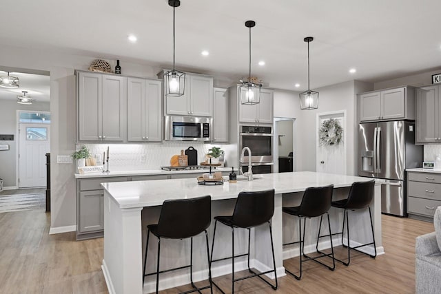 kitchen featuring appliances with stainless steel finishes, gray cabinets, a kitchen island with sink, and pendant lighting