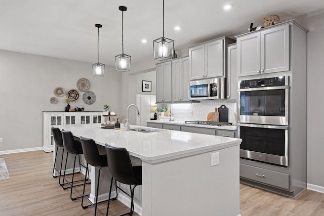 kitchen featuring light stone counters, stainless steel appliances, sink, decorative light fixtures, and a center island with sink