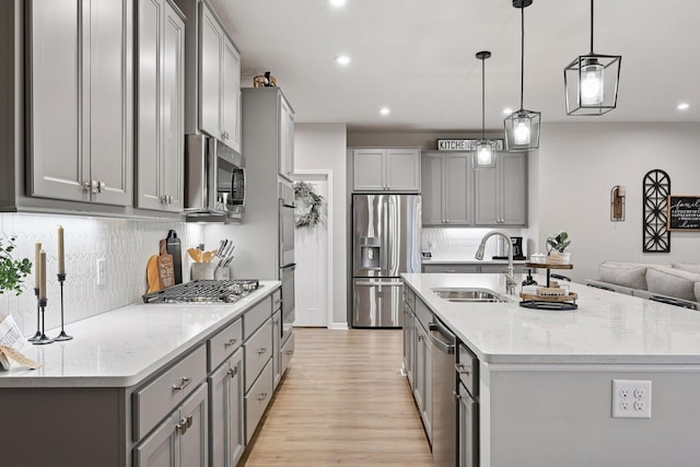 kitchen with gray cabinetry, light stone countertops, hanging light fixtures, a kitchen island with sink, and appliances with stainless steel finishes