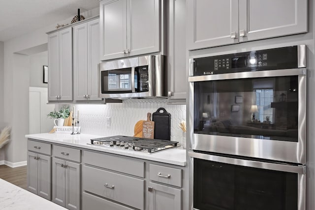 kitchen featuring backsplash, gray cabinets, light stone counters, and stainless steel appliances