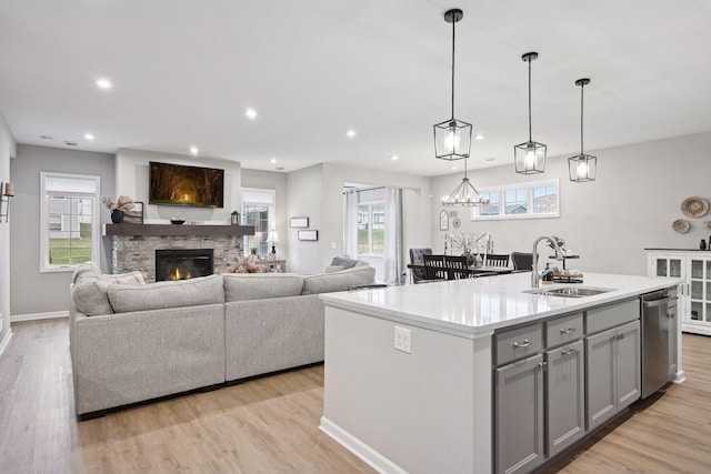 kitchen with gray cabinetry, a kitchen island with sink, a stone fireplace, sink, and hanging light fixtures